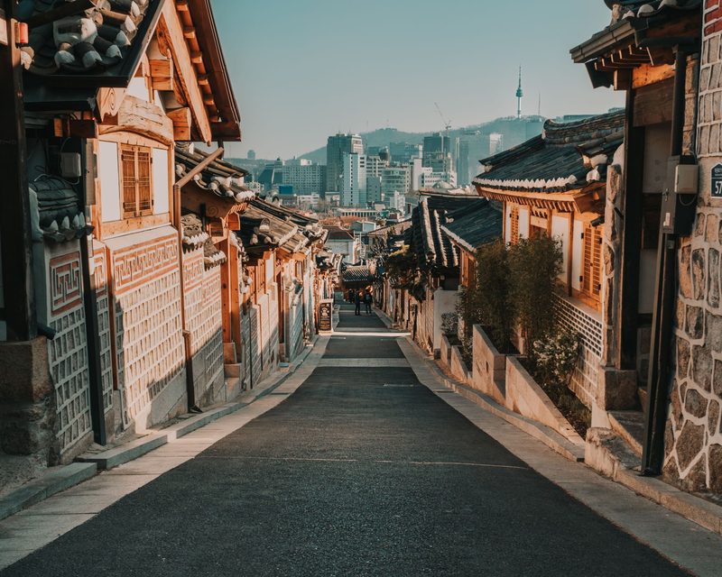 Hanok alley opening to Seoul skyline at sunset