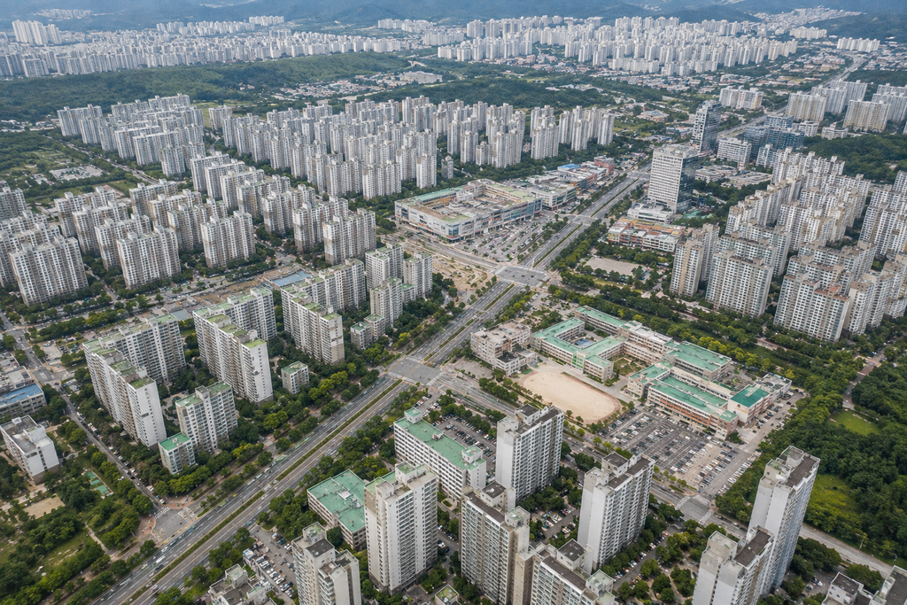 Aerial view of a planned Korean new town with apartment complexes, straight roads, schools, green spaces, parking areas, and commercial districts